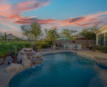 A backyard swimming pool at dusk with a freeform design and rock features on the left side.