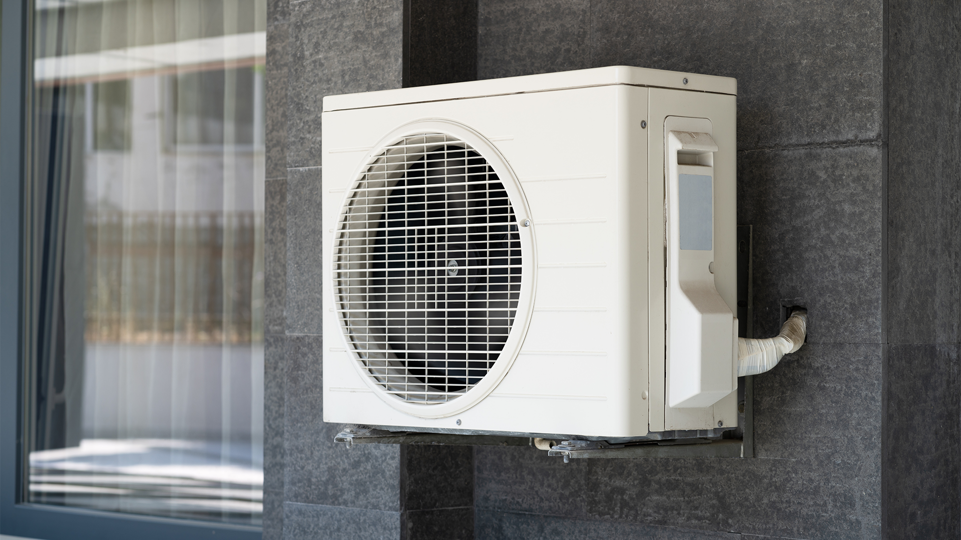 White aquatight heat pump with a large circular fan in front connected to building.